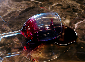 A wine glass tipped over on a dark marble surface with red wine pooling beside it and a reflection in the liquid.