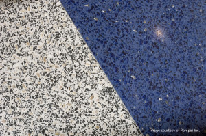 Close-up of a diagonal seam where light gray speckled concrete meets blue speckled asphalt pavement.