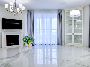 Bright living room with white marble floor, fireplace beneath a wall-mounted TV, a potted plant, and a glass-front cabinet.